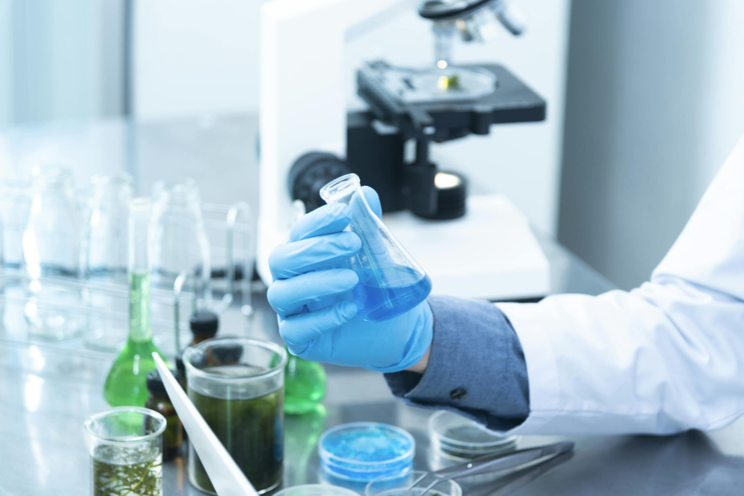 Atrium scientist analyzing liquid formulation in laboratory setting with microscope and glassware under cGMP quality control procedures