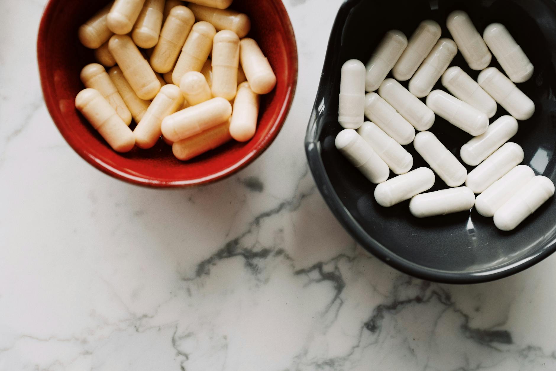 Top view of red and black ceramic bowls filled with assorted capsules on marble surface. — Atrium Scientific Group