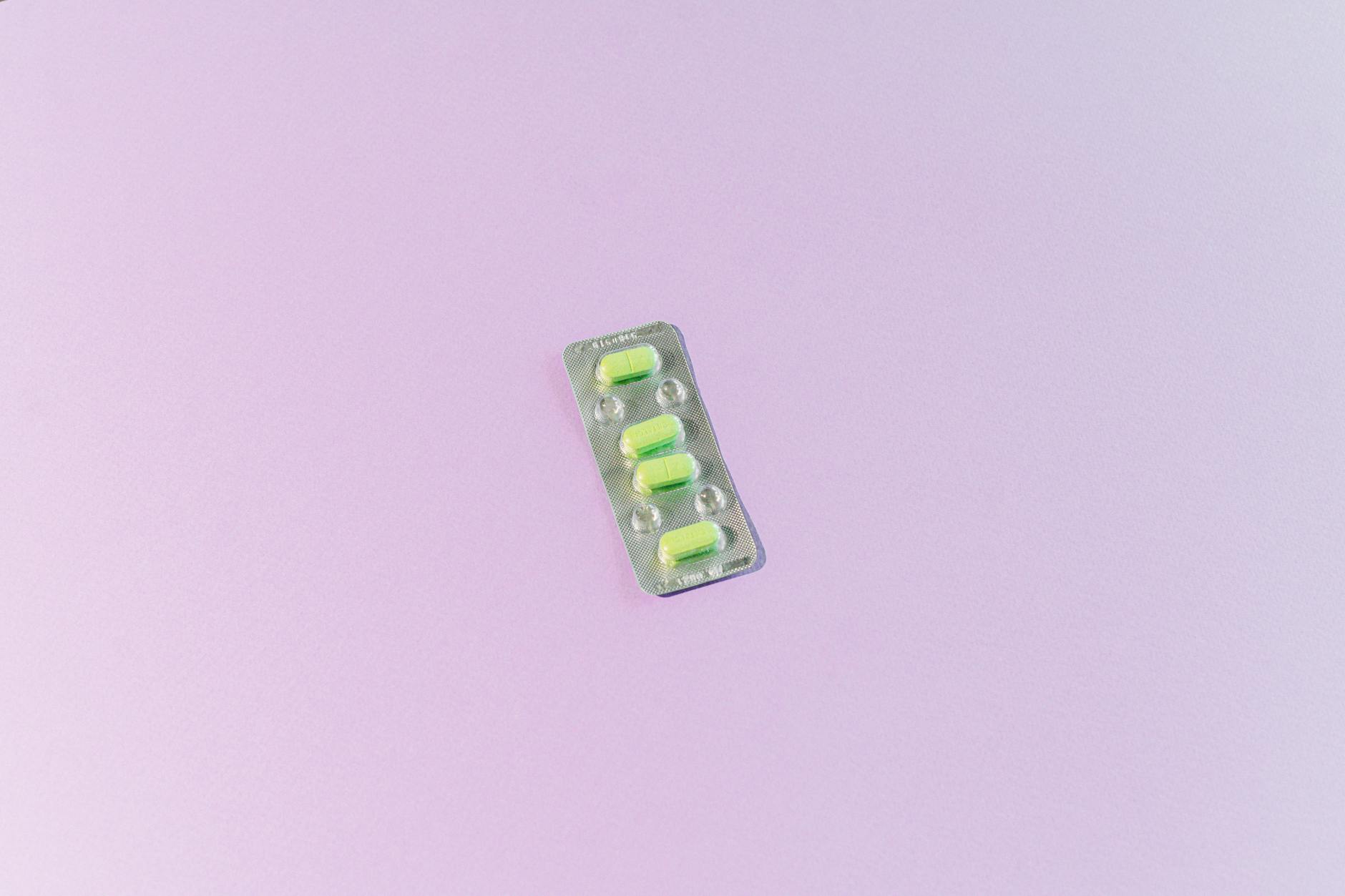 High angle view of blister pack with yellow pills on a light purple background, providing ample copy space. — Atrium Scientific Group