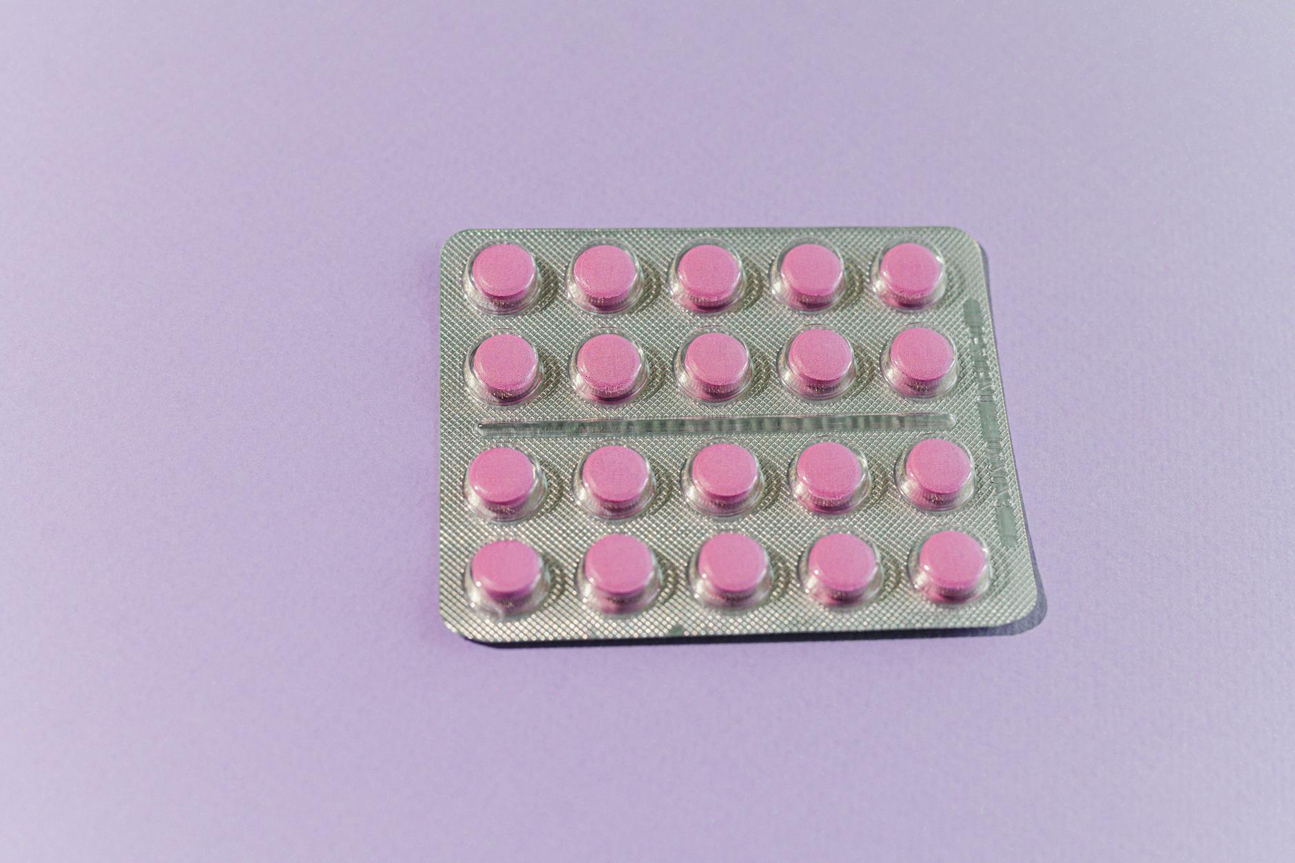 A neatly arranged blister pack containing pink tablets on a solid purple surface. — Atrium Scientific Group