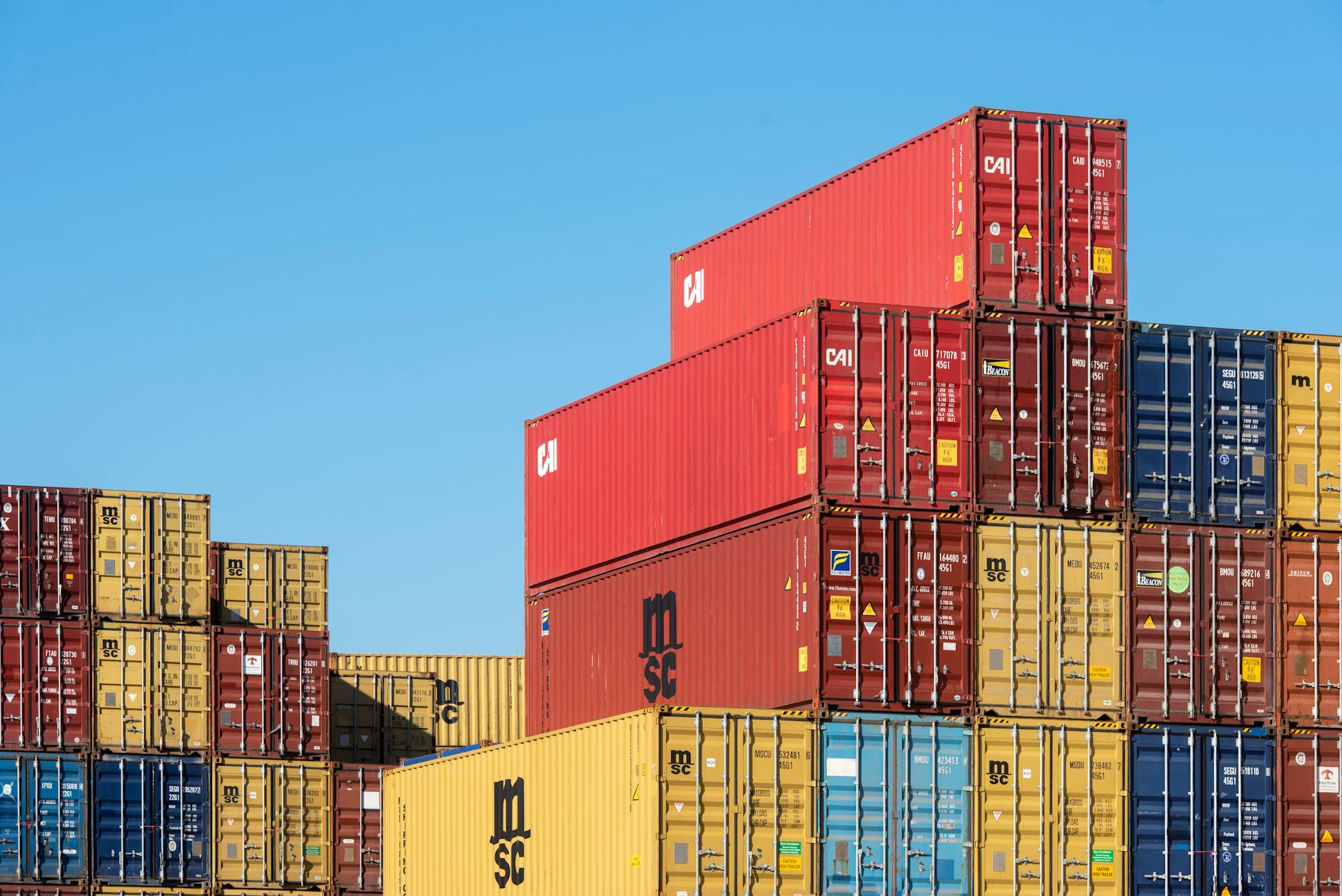 A vibrant collection of stacked shipping containers under a clear, blue sky. Ideal for logistic themes. — Atrium Scientific Group