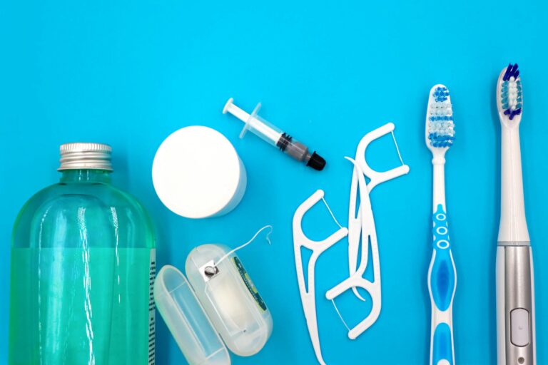Flat lay of oral hygiene essentials including toothbrushes, floss, and mouthwash on a blue surface. — Atrium Scientific Group
