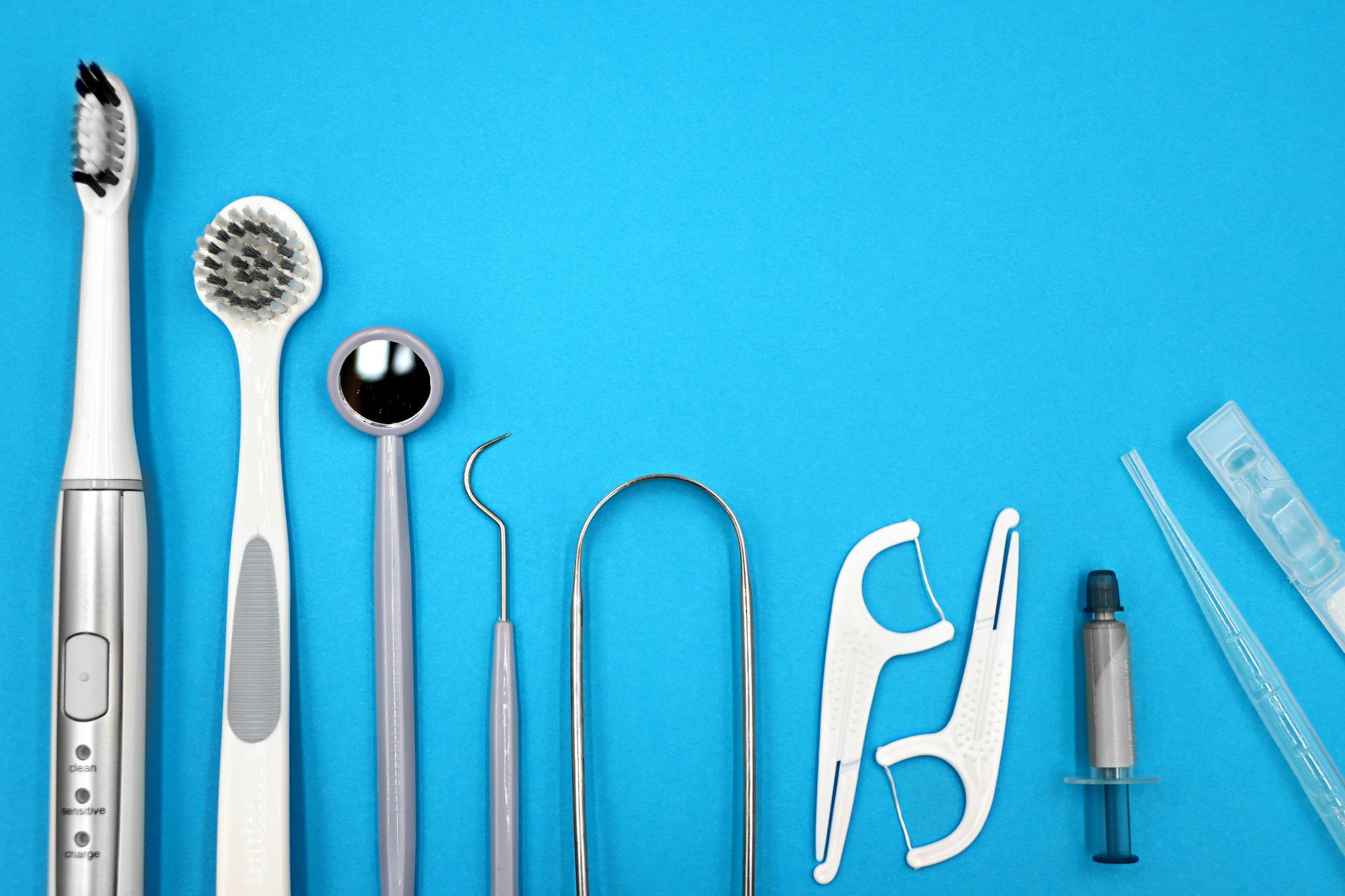 Flat lay of dental care tools including toothbrushes, dental mirror, and floss sticks on blue background. — Atrium Scientific Group