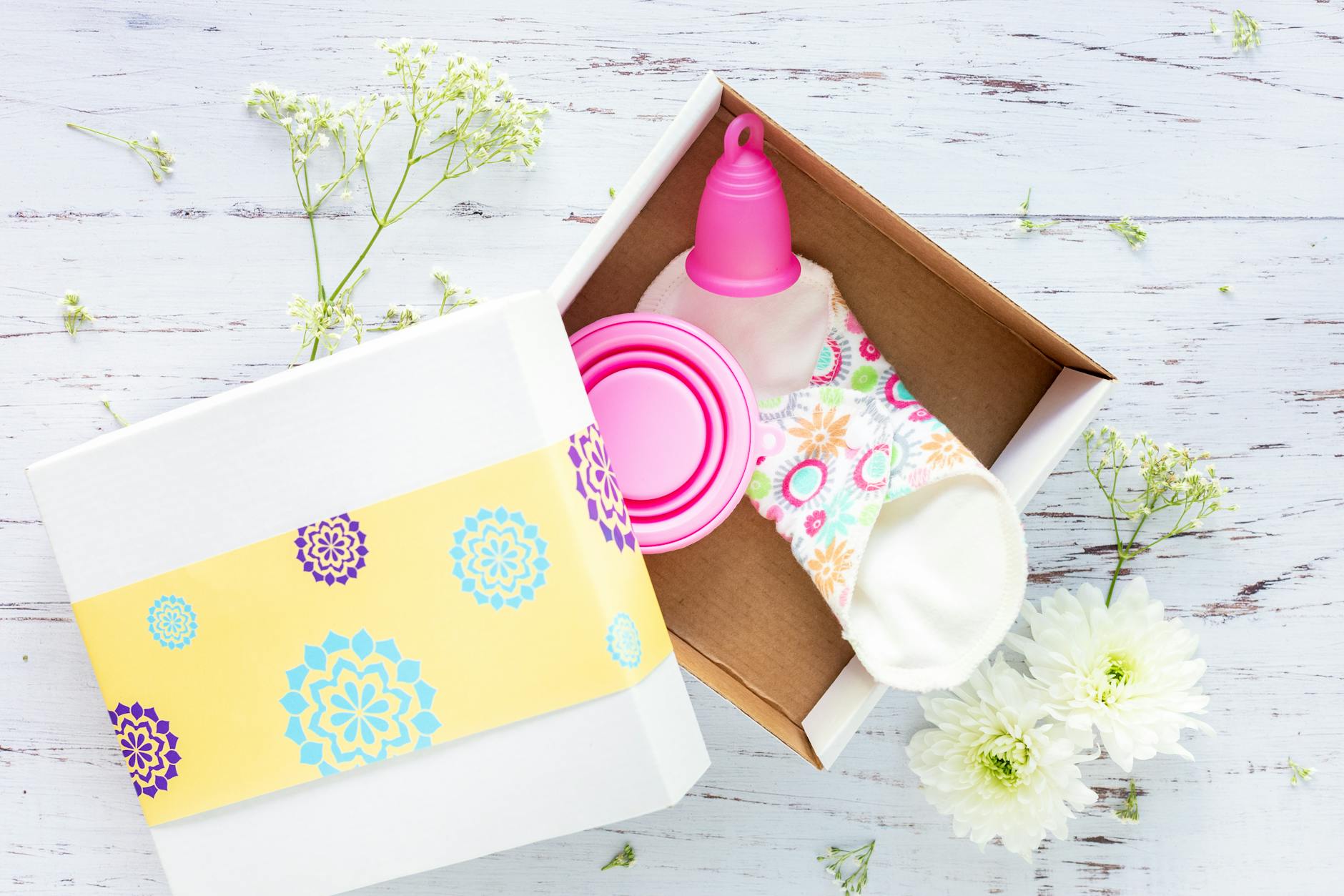 Brightly decorated gift box containing reusable menstrual cup and pads on a rustic background. — Atrium Scientific Group