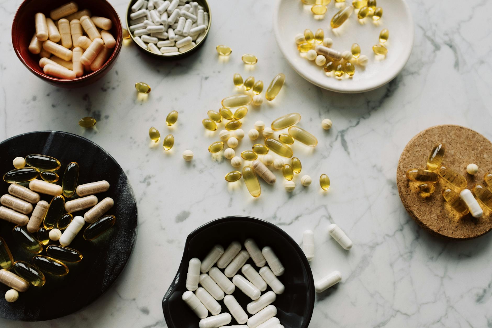 From above of various types of medication pills and yellow capsules of omega placed on different plates and stands on table — Atrium Scientific Group